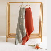 Forest Deer swaddle and terra cotta muslin blanket hanging side by side on rack